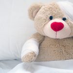 Erste Hilfe bei Kindern: Ein Teddybär ist im Bett und hat einen Verband um seinen Kopf.