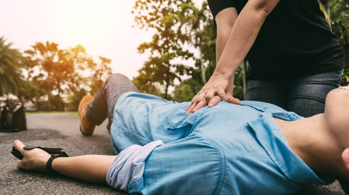 Erste Hilfe: Junger Mann im blauen Hemd liegt auf der Straße. Ein anderer Mann macht mit den Händen Herzdruckmassage. Erste Hilfe: Junger Mann im blauen Hemd liegt auf der Straße. Ein anderer Mann macht mit den Händen Herzdruckmassage.